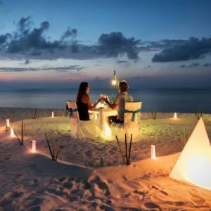 A couple sitting at the beach with candles in front of them.