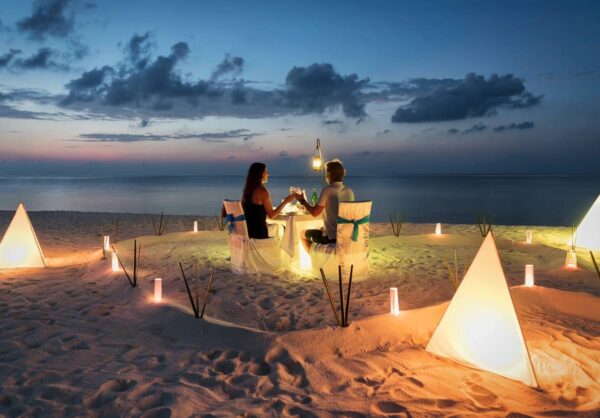 A couple sitting at the beach with candles in front of them.