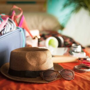 A hat and sunglasses on the bed with a bag