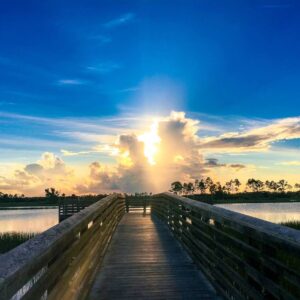 A pier with people walking on it and the sun setting.