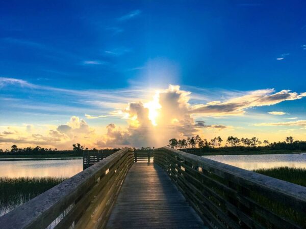 A pier with people walking on it and the sun setting.